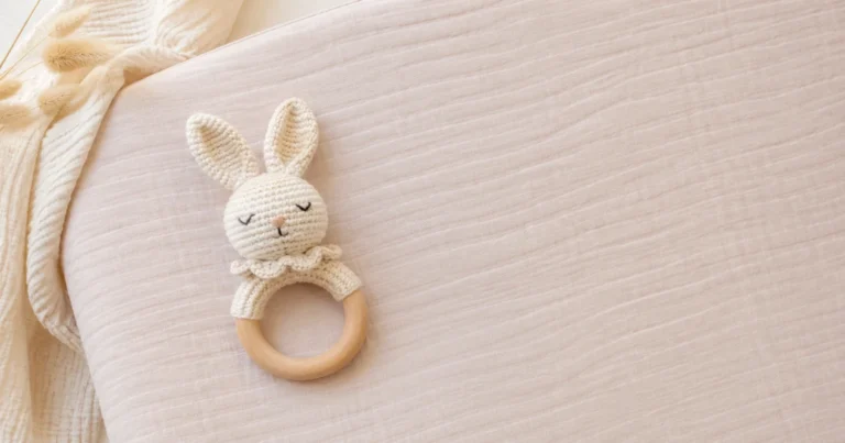 Un anneau de préhension fini avec lapin au crochet, reposant sur un matelas à langer en pastel. Lumière naturelle.