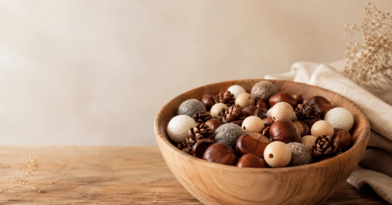 Bol en bois avec un mélange de châtaignes, perles en bois, pommes de pin et boules de laine. Lumière naturelle, tons chauds.