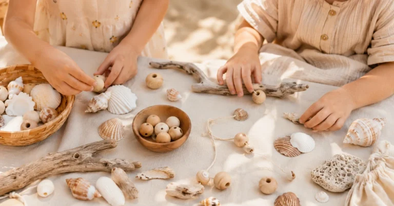 Table de plage avec coquillages, bois flotté, perles en bois, les mains de l'enfant trient. Lumière ensoleillée, ton sable.